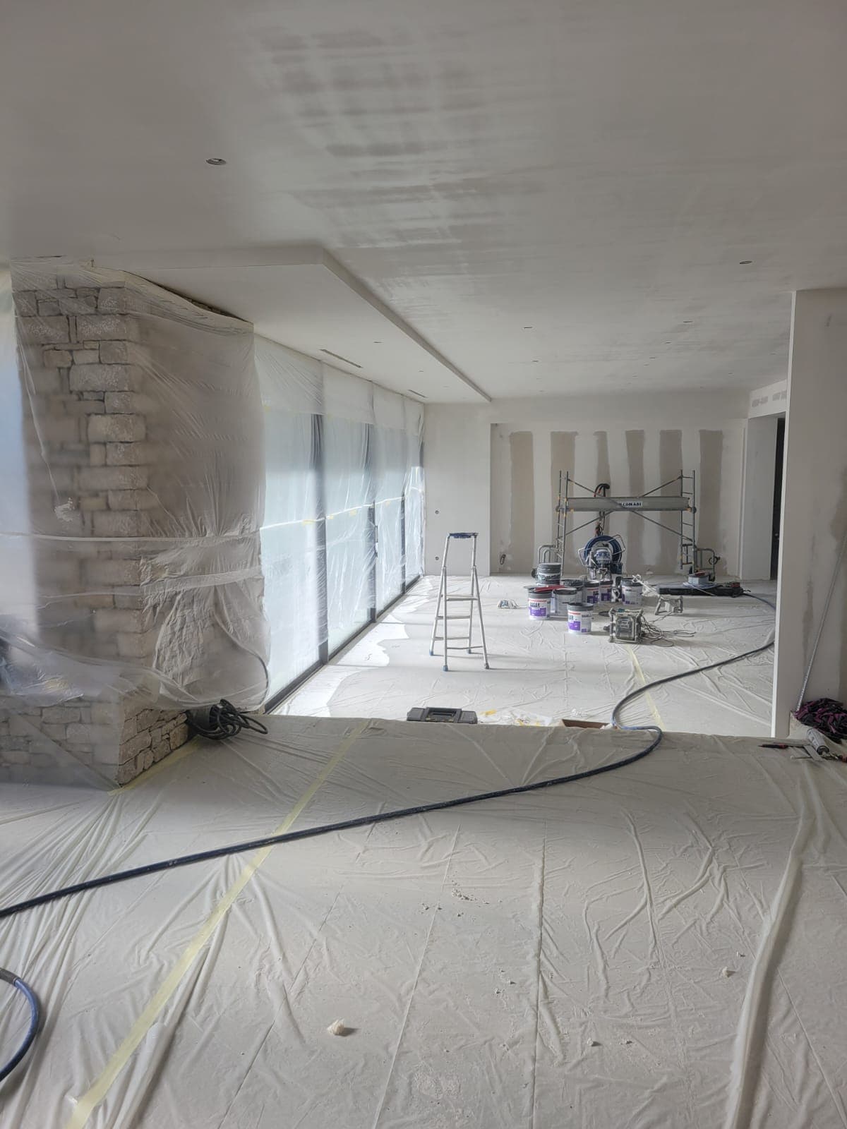 Mur en pierre et baies vitrées protégés par bâches avant travaux de peinture intérieure